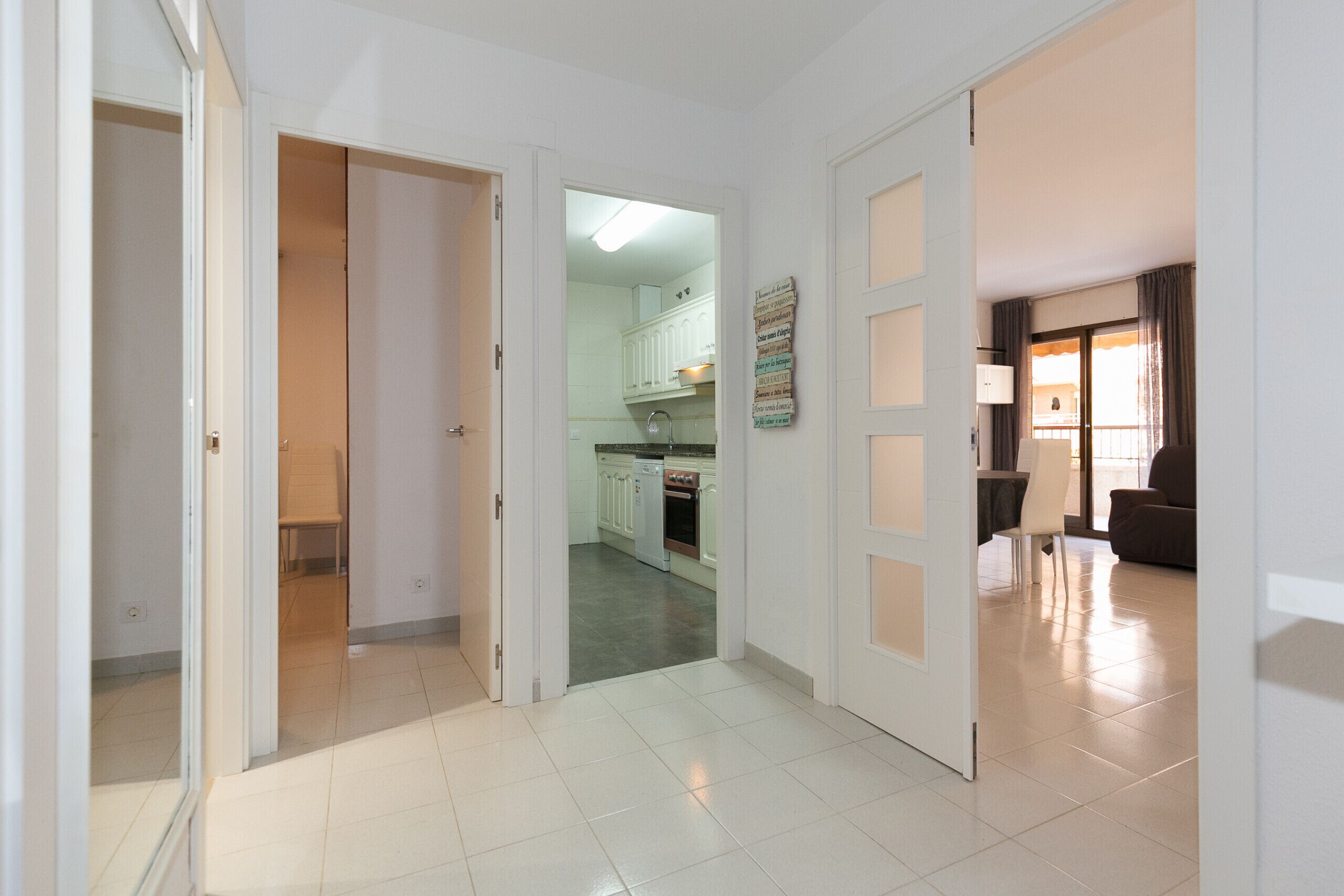 A hallway leading to a kitchen with white cabinets and a dining area with a table and chairs.