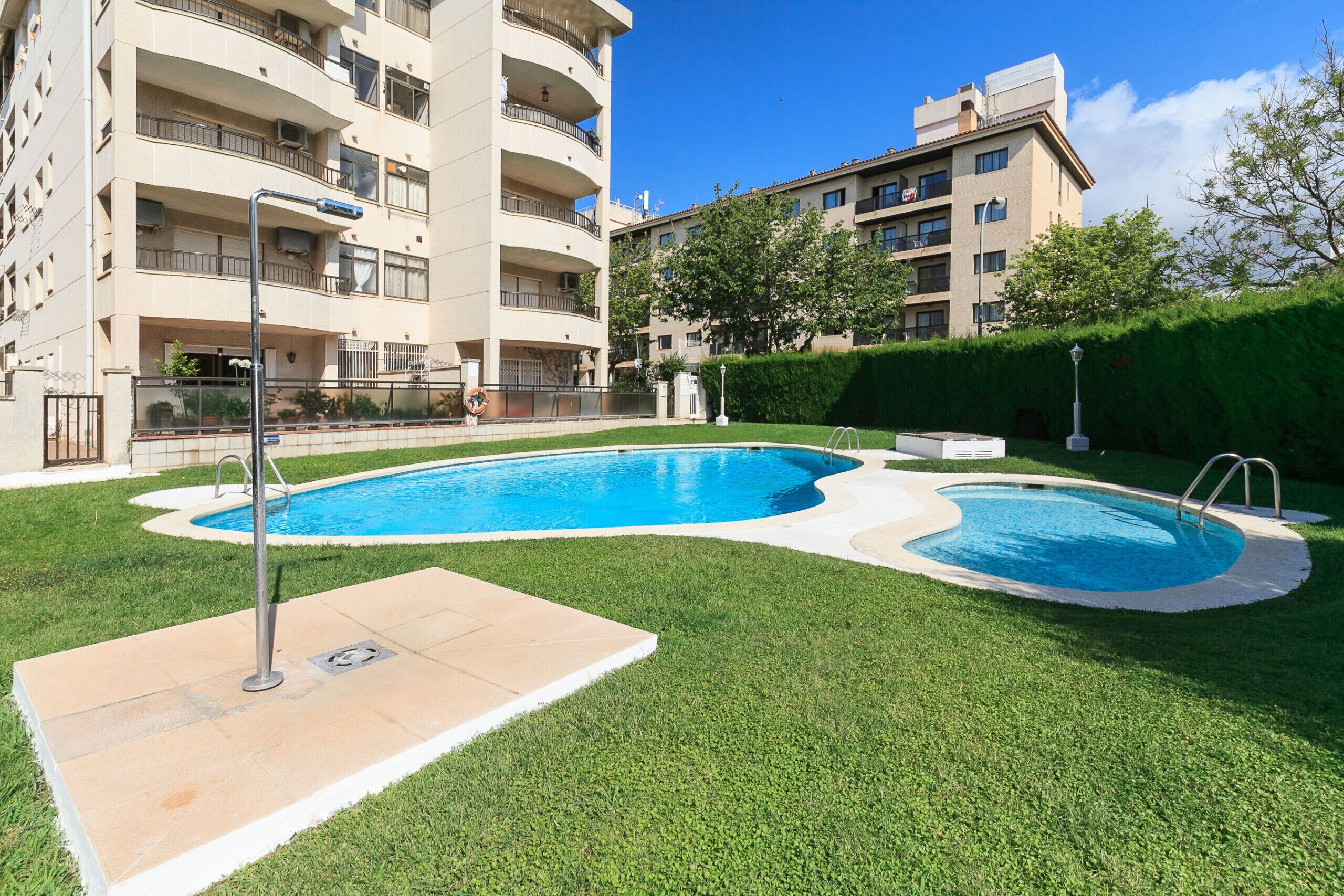 A swimming pool with a surrounding grassy area and a multi-story building in the background.