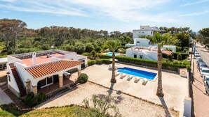 Eine moderne Villa mit Swimmingpool, einer überdachten Terrasse und Blick auf die umliegende Grünfläche und Hügel.