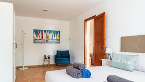 Ein Hotelzimmer mit einem Bett, einem Segelbootgemälde, einem blauen Sessel und einem Kissen mit der Aufschrift "Beach House".