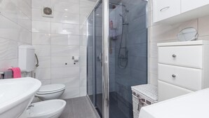 Un baño moderno con ducha acristalada, lavamanos blanco, inodoro y mueble blanco.