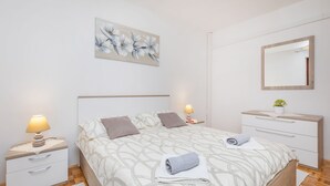Un dormitorio ordenado con cama, mesitas de noche, cómoda, espejo y una obra de arte floral en la pared.