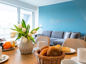 Une pièce avec un mur bleu, un canapé gris, une table avec des aliments pour le petit-déjeuner et un vase de tulipes blanches.