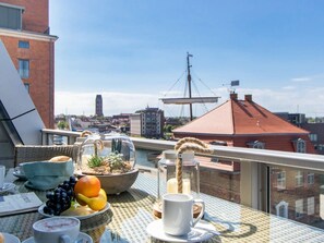 A balcony with a table set for breakfast, including fruits, a coffee cup, and a candle.