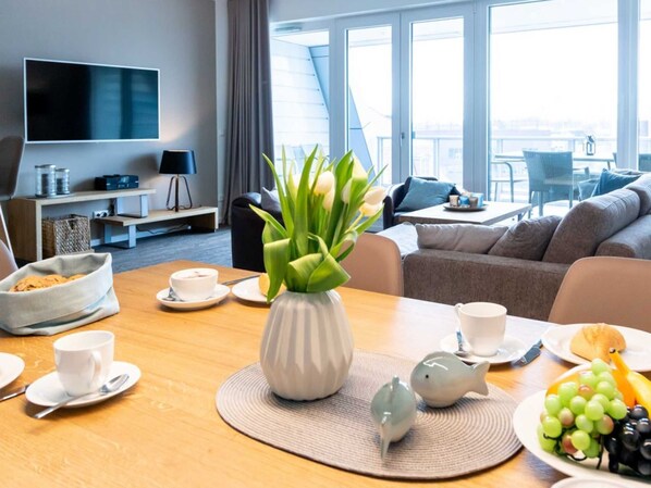A modern hotel room with a dining area, a sofa, a TV, and a view of the city.