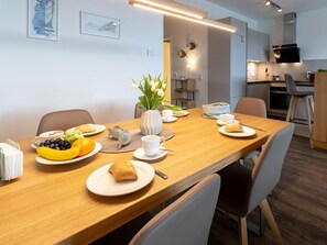 A dining area with a wooden table set for breakfast, including plates of food, cups, and a vase with flowers.