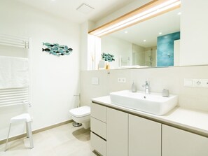A modern bathroom with a white sink, mirror, and toilet.