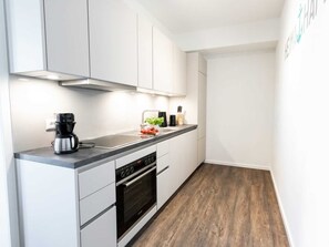 A modern kitchen with white cabinets, a black countertop, a coffee maker, and a wooden floor. - Hafenspitze App. 30, Deutschland (Wismar)