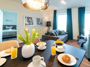 A dining table with breakfast items, a vase with flowers, and a bed in the background. - Hafenspitze App. 30, Deutschland (Wismar)