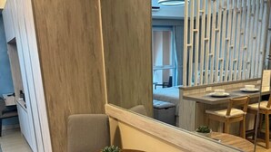 A modern dining area with a round wooden table, a potted plant, and a mirror reflecting the room. - Honeymoon Suite (Tagaytay)