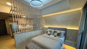 A modern bedroom with a large bed, a bench, a wall-mounted light, and a decorative partition. - Honeymoon Suite (Tagaytay)