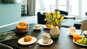 Een eetruimte met een ontbijttafel, een bloevas en een aan de muur bevestigde televisie.