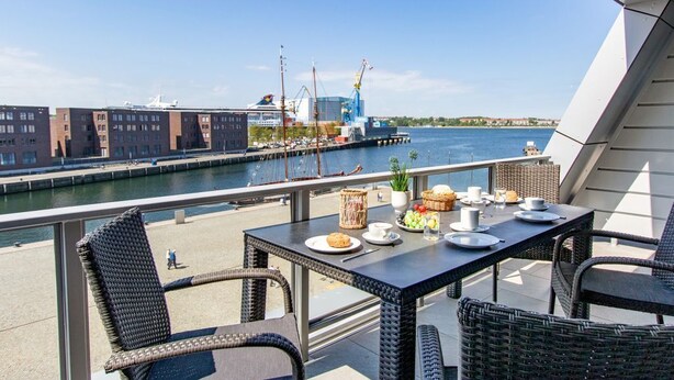 Een balkon met rieten meubels, een tafel gedekt met borden, kopjes en een mand vol fruit.