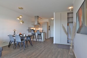 A modern kitchen with white cabinets, a dining area with grey chairs, and a large mirror above the counter. - Hafenspitze App. 35, Deutschland (Wismar)