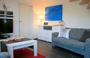 A living room with a flat-screen TV, a white coffee table, a grey sofa, and a blue artwork on the wall.