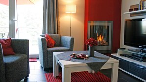 Una sala de estar moderna con dos sillones grises, una mesa de centro blanca, una chimenea y un televisor de pantalla plana.