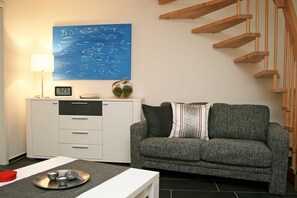A modern living room with a grey sofa, a white cabinet, a blue fish painting, a clock, and a staircase.