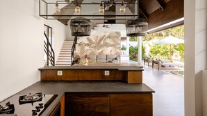 A modern kitchen with a central island, a staircase, and a view of an outdoor patio area. - Contemporary Private Villa, 4 BR, Canggu With Staff (Canggu)