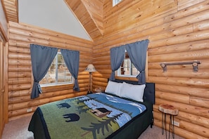 Une chambre dans une cabane en rondins, avec un lit, des rideaux, une table de chevet et une fenêtre.