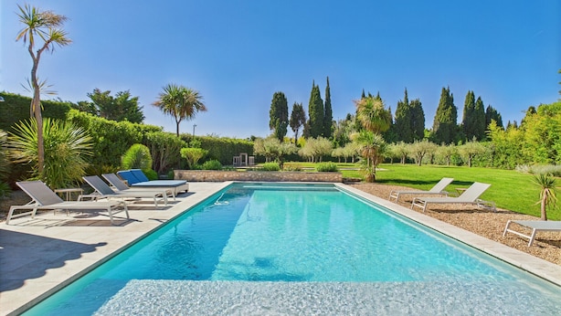 Una piscina rectangular con agua azul cristalina, rodeada de sillas de descanso y un jardín cuidado con diversas plantas y arbustos.