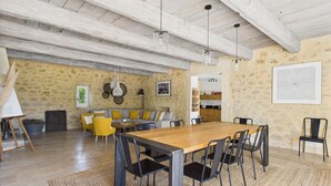 Un comedor amplio con una larga mesa de madera y sillas negras, un sofá amarillo y una pared de piedra con un cuadro enmarcado.