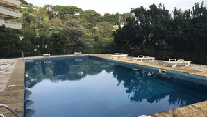 A rectangular swimming pool with clear blue water, surrounded by a stone deck and a metal fence. There are white lounge chairs along the poolside. - Pierre Longue,3 bedrooms apartment with sea view in bulding with swimming pool (Cannes)