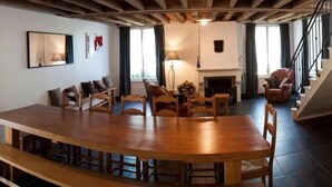 Een ruime woonkamer met een houten eettafel, stoelen, een open haard en een trap.