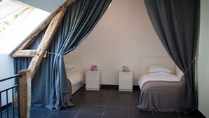 Een slaapkamer met een schuine kap, twee nachtkastjes, een bed en een raam met gordijnen.