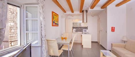 Een moderne woonkamer met een eethoek, kitchenette en een groot raam met gordijnen.