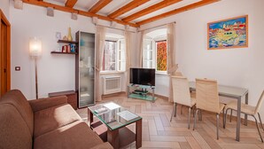 A living room with a sofa, TV, glass coffee table, and dining area with chairs.