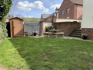 Enjoy outdoor dining or relaxation in this serene backyard with a lawn, wooden table, and benches.