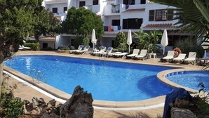 A swimming pool with lounge chairs and umbrellas, surrounded by a stone wall and greenery. - Modern apartment with a fantastic view Vistamar 3 (Cala en Porter)