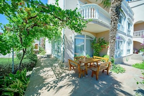 Relax in a serene courtyard surrounded by lush greenery and a palm tree, with a balcony and stone wall.