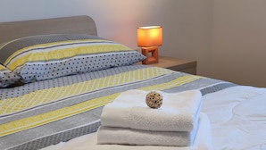 A neatly made bed with a white duvet, a decorative wooden object, and a lamp on a bedside table.