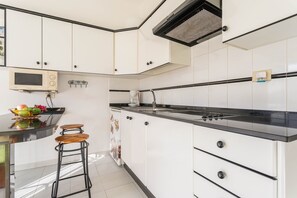 A kitchen with white cabinets, a black countertop, a microwave, a kettle, and a fruit bowl.