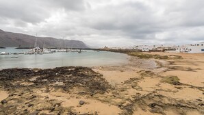 Uma área costeira com barcos, uma praia de areia e edifícios ao fundo.