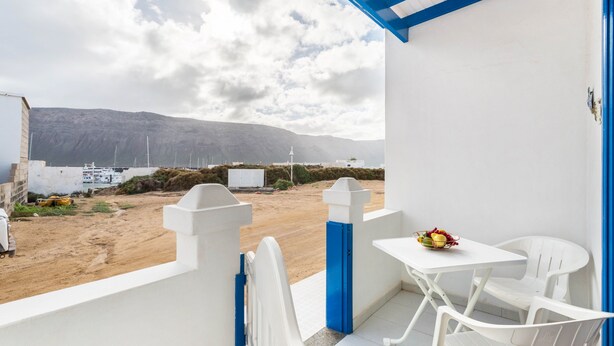 Varanda com mobiliário branco e azul, uma mesa com frutas e vista para a praia e montanhas.