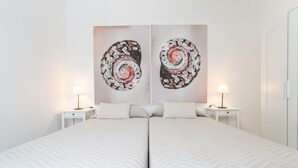 Uma cama de casal com colcha estampada em padrão herringbone, duas mesas de cabeceira com abajures e duas obras de arte abstratas na parede.