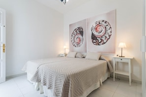 Un dormitorio con una cama, dos mesitas de noche, una puerta y dos cuadros colgados en la pared.