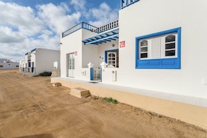 Una hilera de edificios blancos con detalles azules y un camino de tierra al frente.