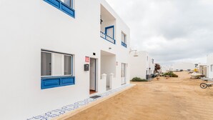 A white building with blue accents, a sandy ground, and a clear sky. - Holiday Home "El Sombrerito 5" with Terrace & Wi-Fi (Caleta de Sebo)