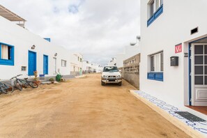 Una calle estrecha con edificios blancos, puertas azules y un coche estacionado.