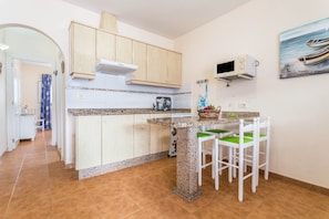 Una cocina con armarios de madera, encimera de granito, microondas y un cuadro de barcos en la pared.