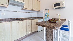 Una cocina con armarios de madera, encimera de granito, microondas y un pequeño comedor con sillas azules.