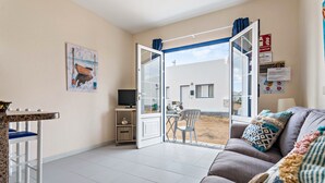 Sala de estar con sofá, mesa de comedor, televisor y puerta que da a un espacio exterior.