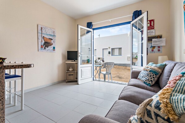 A living room with a sofa, a dining table, a TV, and a door leading to an outdoor area.