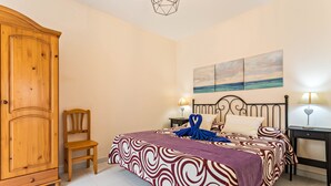 Un dormitorio con cama, armario de madera, silla, mesita de noche y un cuadro en la pared.