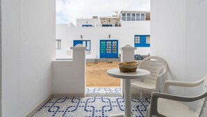 A balcony with a view of a blue and white building, a small table with chairs, and a patterned floor. - Holiday Home "El Sombrerito 4" with Terrace & Wi-Fi (Caleta de Sebo)