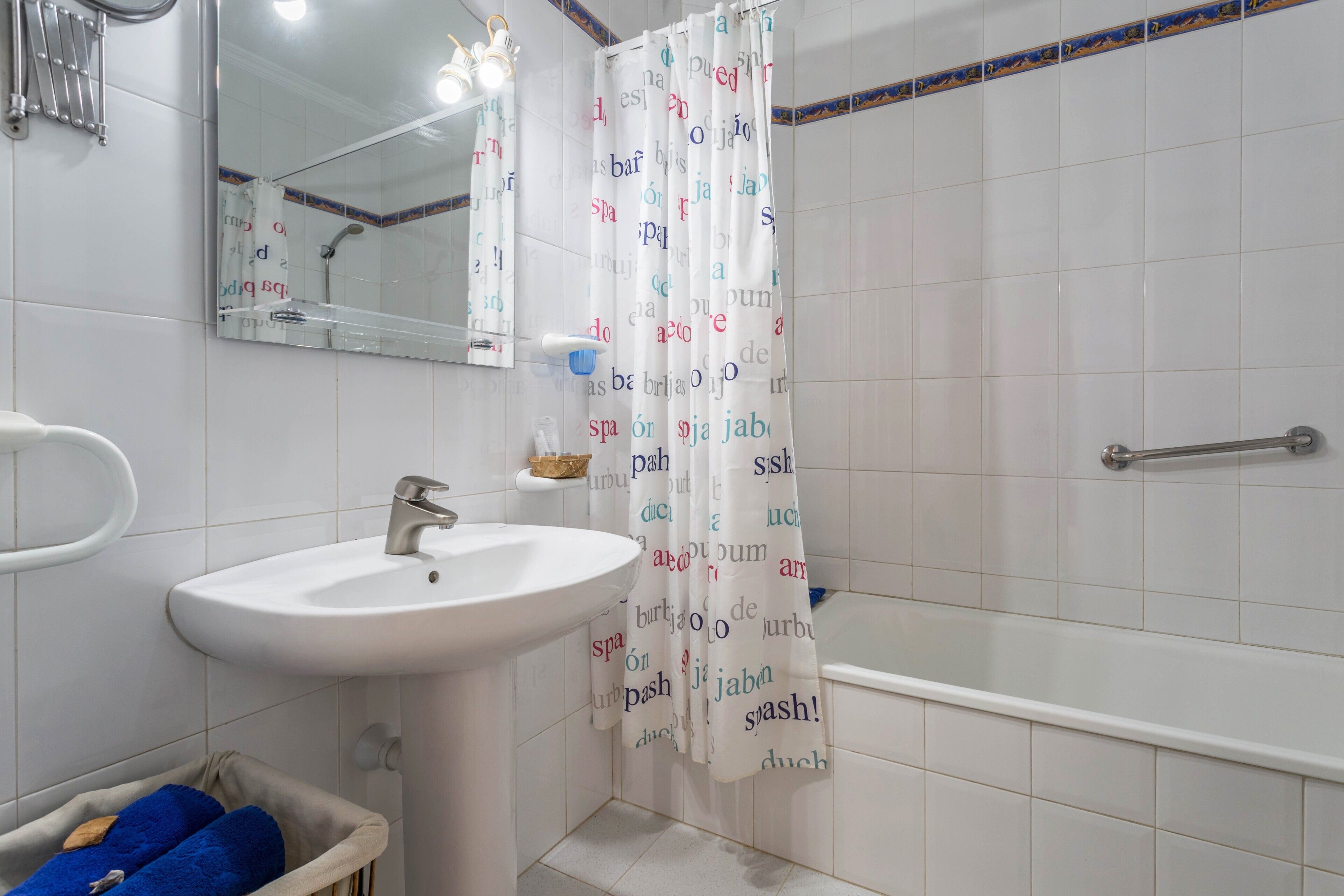 A bathroom with a sink, mirror, shower curtain, and a grab bar.