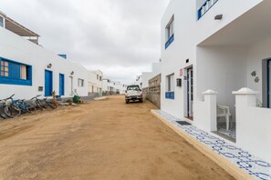 Eine enge Straße mit weißen Gebäuden, blauen Türen und einem abgestellten Fahrzeug.